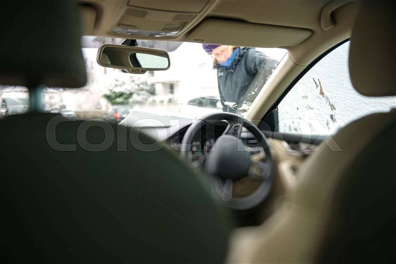 Businesswoman cleaning the right driven car windshield from snow after a snow storm - view from inside the car , stock photo