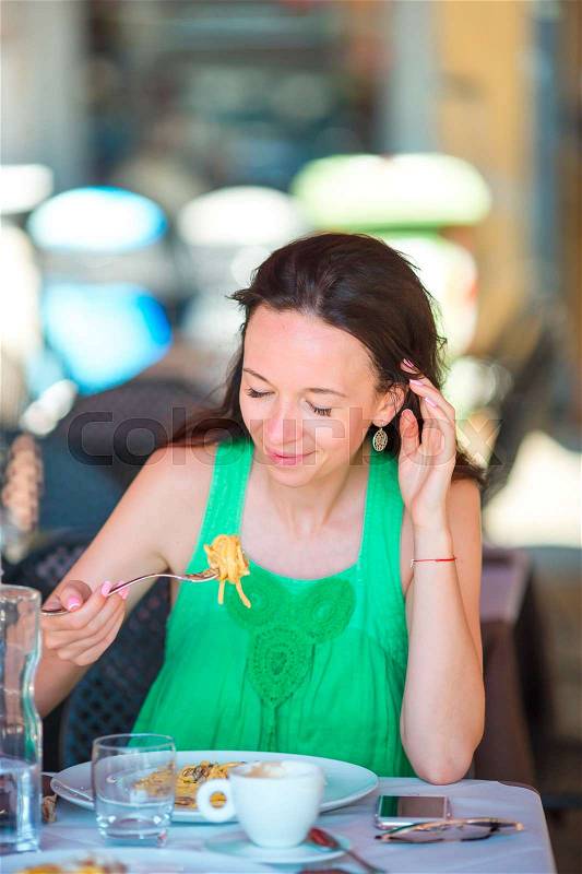 Young woman eating spaghetti at outdoor cafe on italian vacation, stock photo