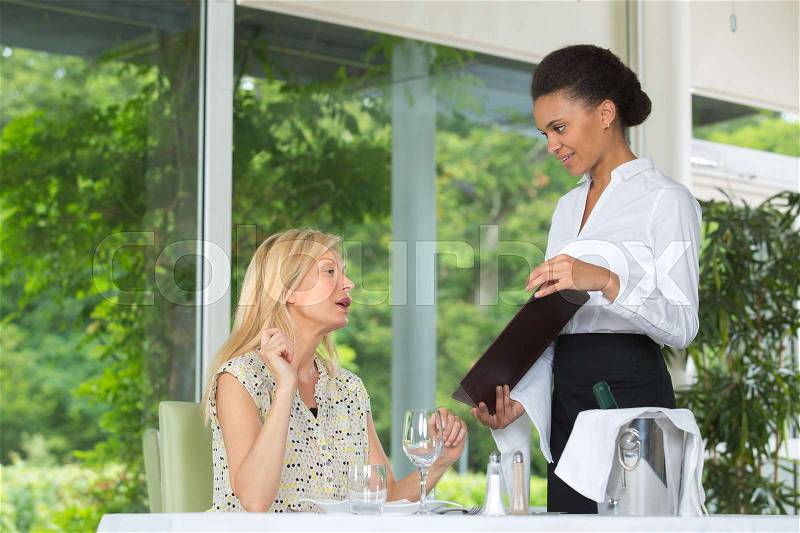 Waitress showing menu to female diner, stock photo