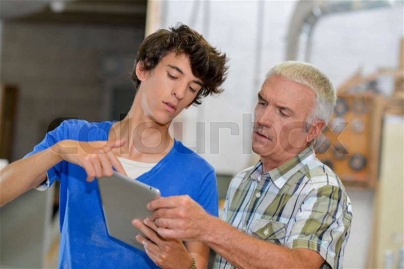 Young man showing older man something on a tablet, stock photo