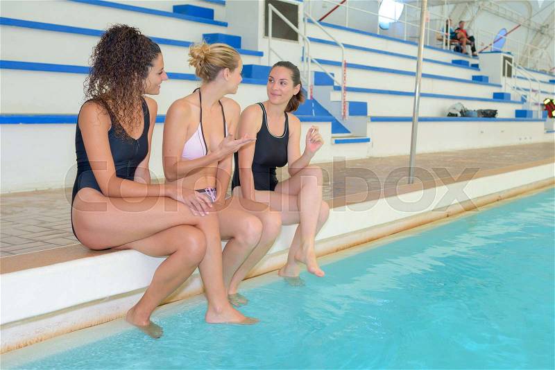 Three young women sat on side of indoor pool, stock photo