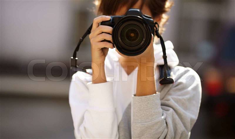 Female photographer with professional SLR camera, natural light, selective focus on nearest part of lens with blend, stock photo