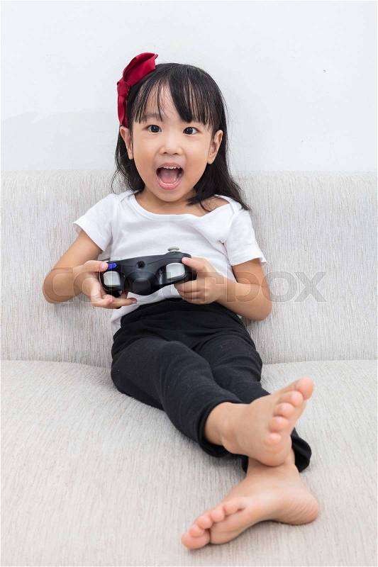 Asian Chinese little girl playing TV games on the sofa in the living room at home alone, stock photo