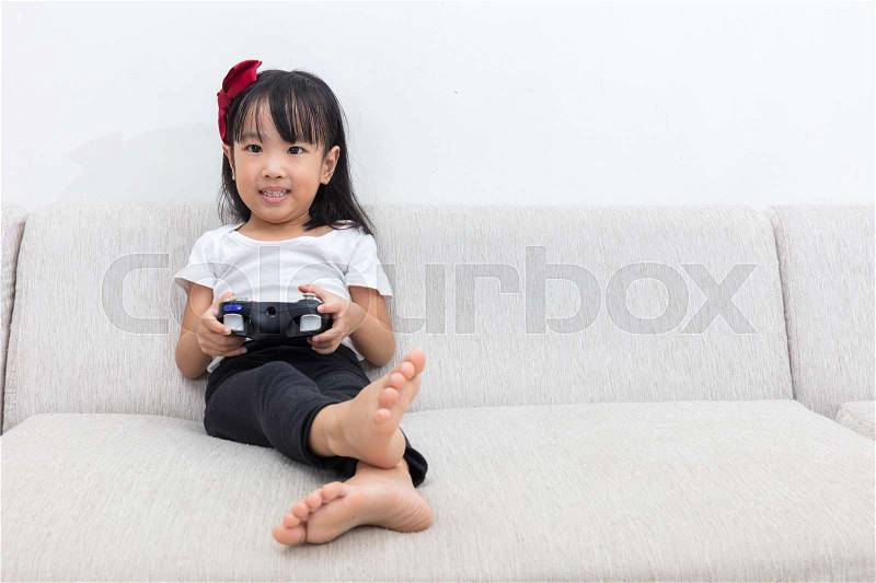 Asian Chinese little girl playing TV games on the sofa in the living room at home alone, stock photo