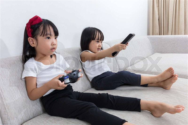 Asian Chinese little sisters playing TV games on the sofa in the living room at home, stock photo
