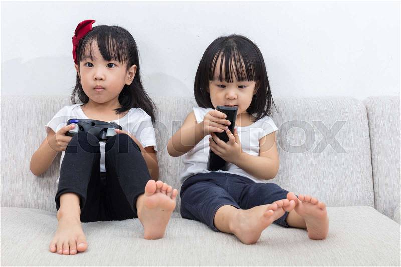 Asian Chinese little sisters playing TV games on the sofa in the living room at home, stock photo