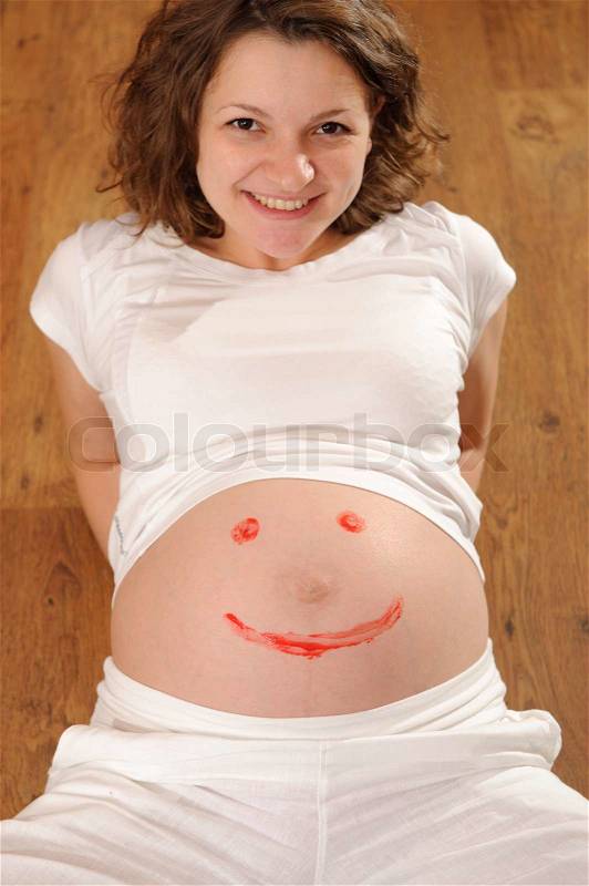 Young pregnant standing with smile sign painted on belly, stock photo