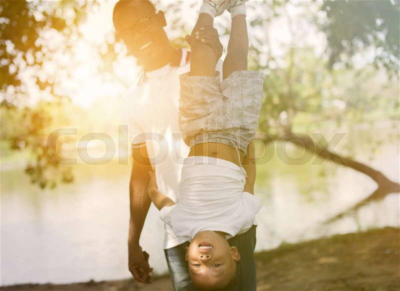 Dad holding a son upside down in park under sunlight, stock photo