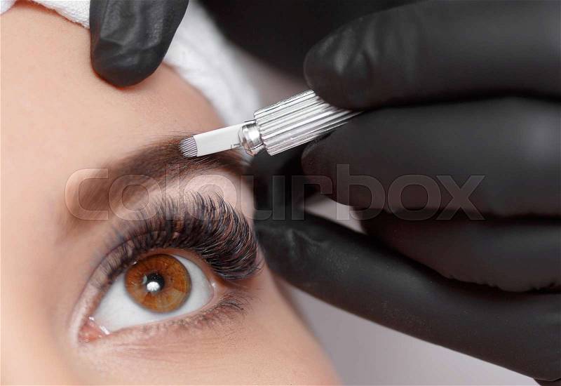 Permanent makeup eyebrows. Mikrobleyding eyebrows workflow in a beauty salon. Cosmetologist applying a special permanent makeup on a woman\'s eyebrows, stock photo