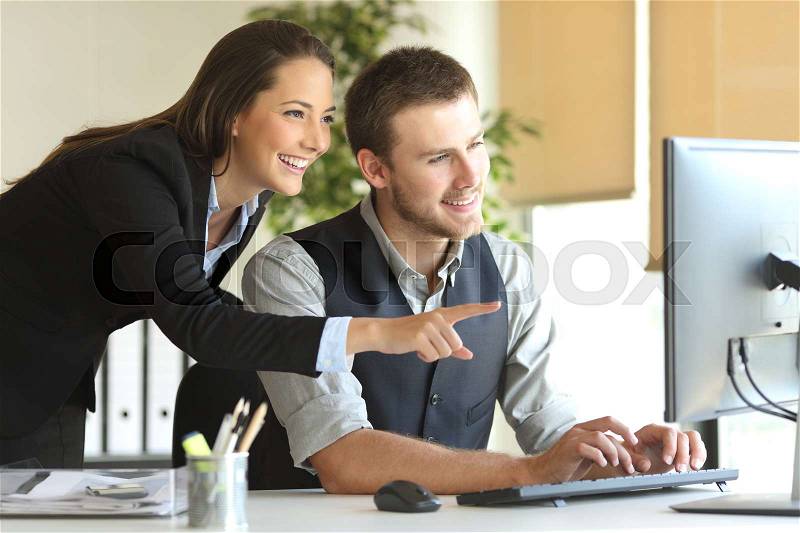 Coworkers working on line with a desktop computer in a desktop at office with a window in the background, stock photo