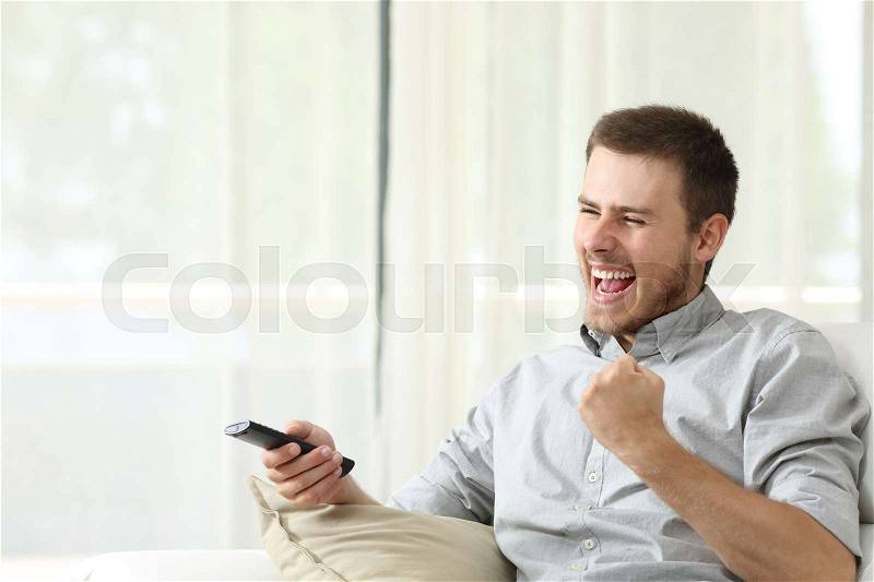 Excited casual man watching tv sitting in a couch at home, stock photo