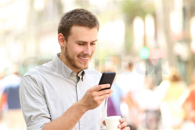 Happy man wearing shirt walking and using a smart phone in the street, stock photo