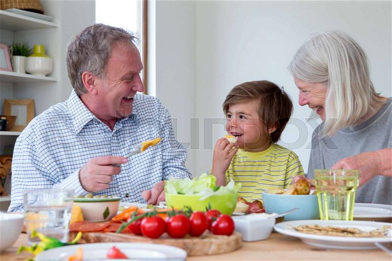 Little boy is eating lunch with his grandparents. They are enjoying a mediterranean style platter, stock photo