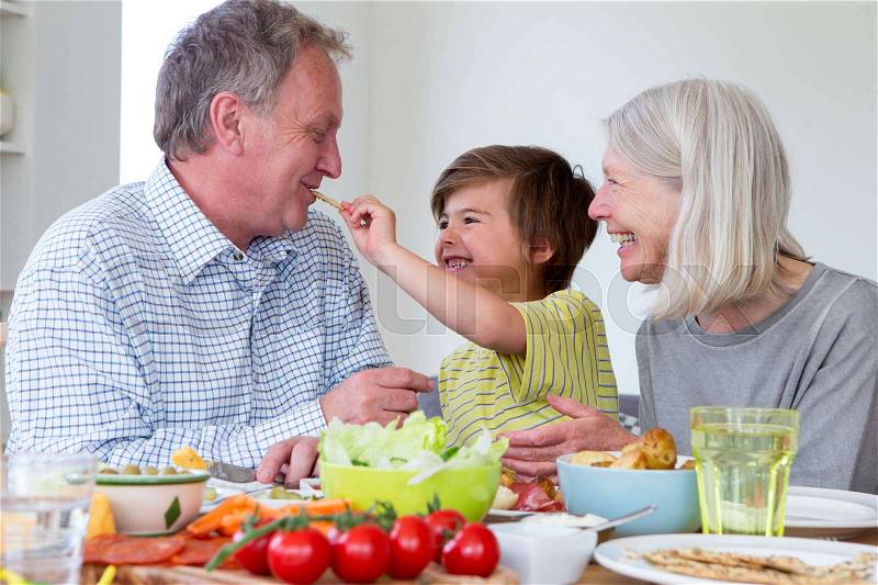 Little boy is feeding his grandfather a cream cracker while having a mediterranean style lunch with both grandparents. , stock photo