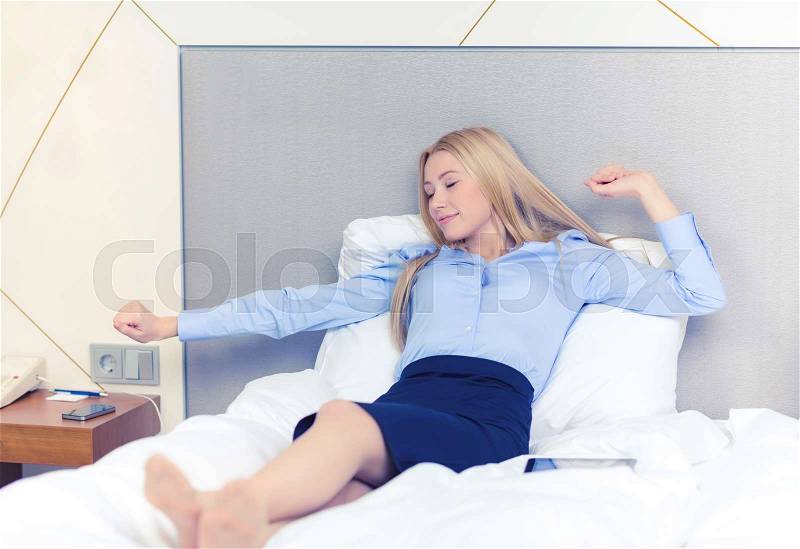 Business, technology, internet and hotel concept - happy businesswoman lying in bed in hotel room, stock photo