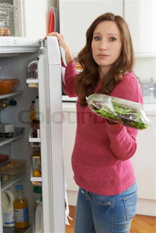 Woman Checking Sell By Date On Salad Bag In Refrigerator, stock photo