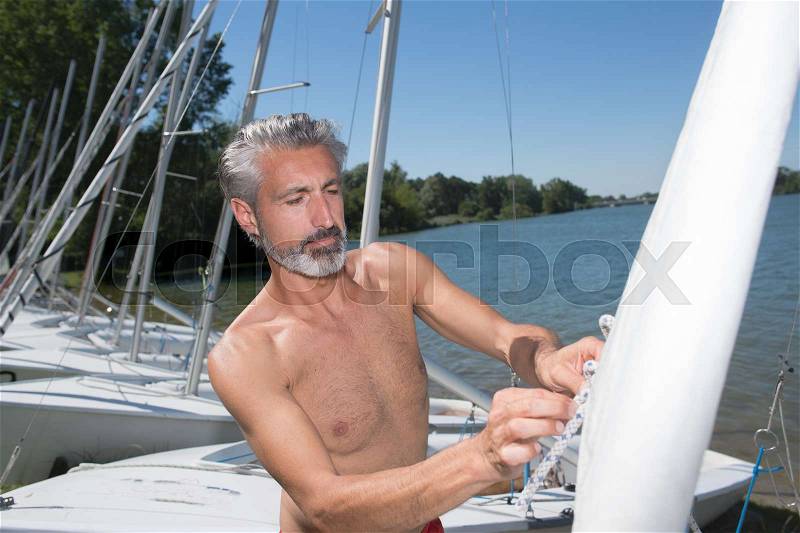 Attractive middle-aged man preparing sport sailboat, stock photo