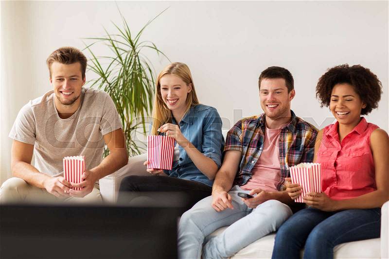 Friendship, junk food, people and entertainment concept - happy friends eating popcorn and watching tv at home, stock photo