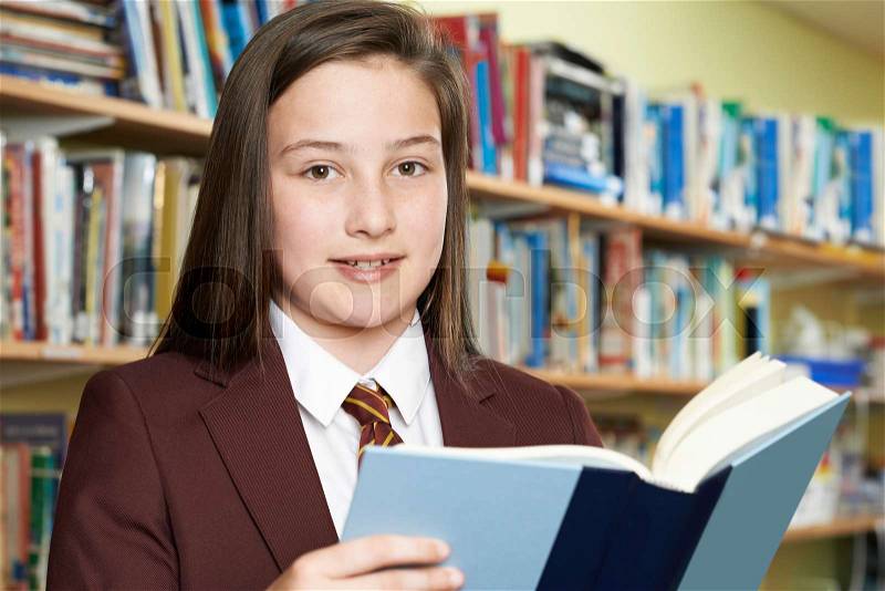 Girl Wearing School Uniform Reading Book In Library, stock photo