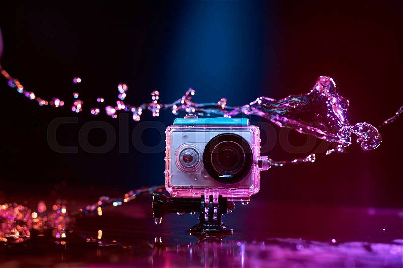 Concept: gear, gadget, action lifestyle, millennial. Vivid colorful shot of action camera in waterproof case splashed with water. Time freeze, stock photo