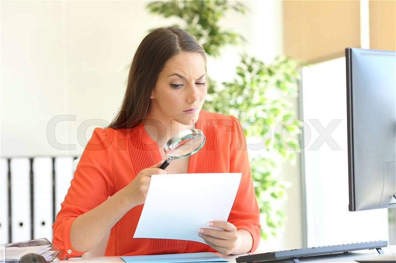 Businesswoman examining a contract meticulously with a magnifying glass at office, stock photo