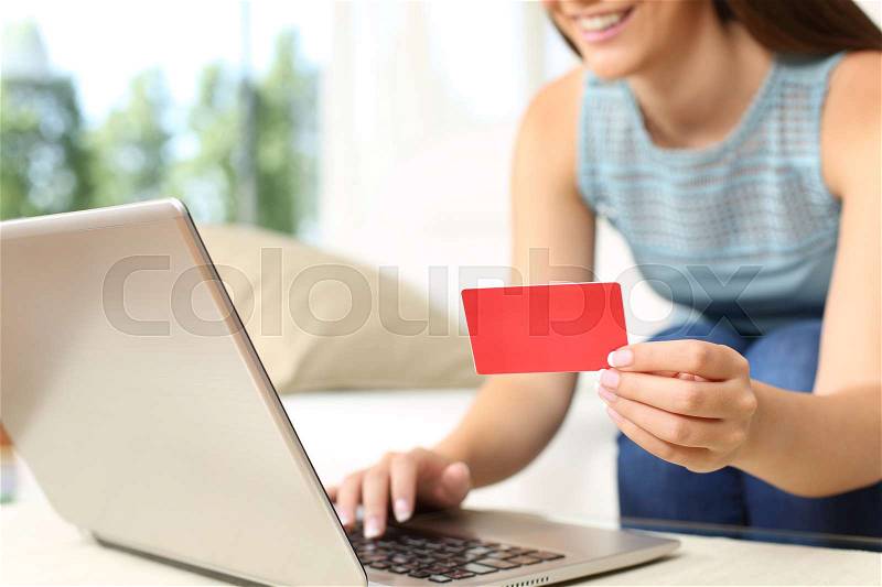 Close up of a woman buying on line with bank card and a laptop sitting on a couch in the living room at home with a window in the background, stock photo