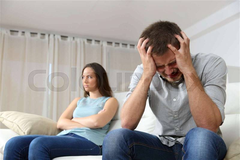 Sad man and his angry girlfriend after argument sitting on a couch at home, stock photo