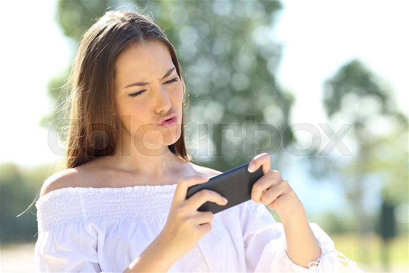 Amazed girl playing games on line with a smart phone in a park, stock photo