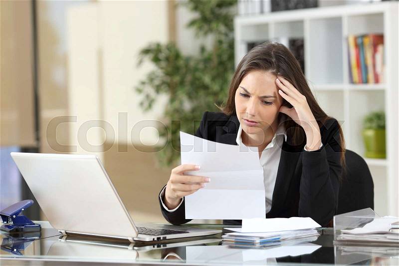 Worried businesswoman reading a notification sitting in a desktop at office, stock photo