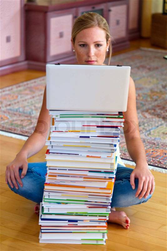A student sits in front of a stack of books and a laptop computer, stock photo