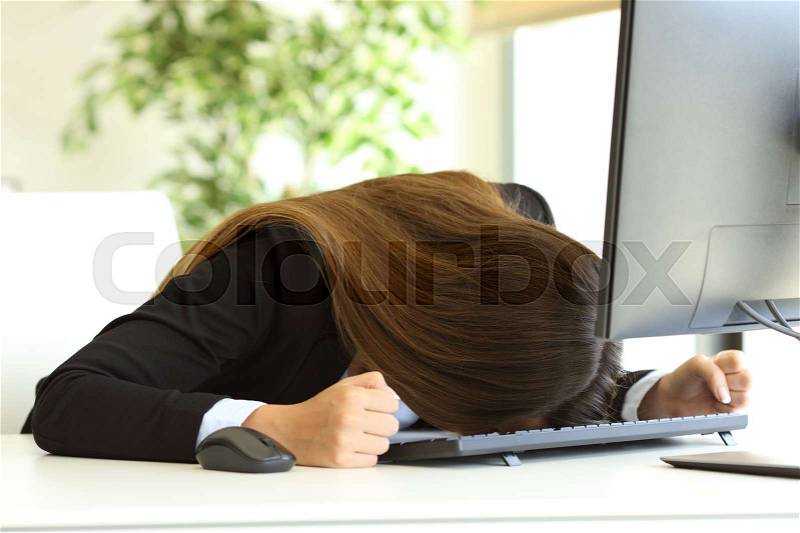 Frustrated businesswoman banging head against the desktop in front of a pc in her workplace, stock photo