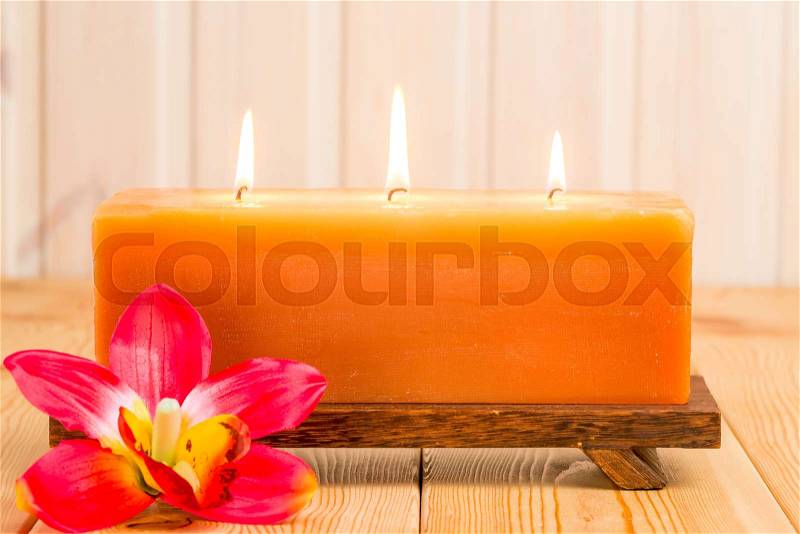 Big burning candle and tropical flower on a wooden table, stock photo
