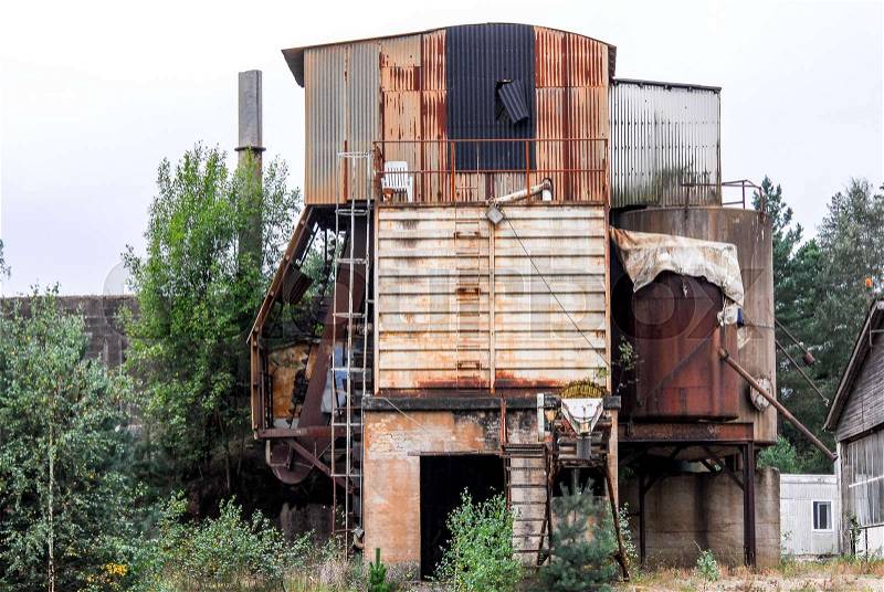 Old abandoned defaulted industrial building which stands with rusty and empty silo, stock photo