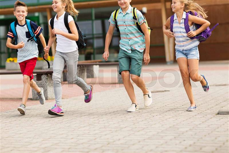 Primary education, friendship, childhood and people concept - group of happy elementary school students with backpacks running outdoors, stock photo
