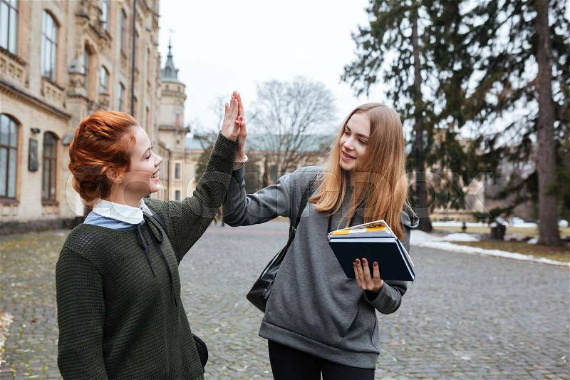 Portrait of a two young girl students giving high five outside the campus, stock photo