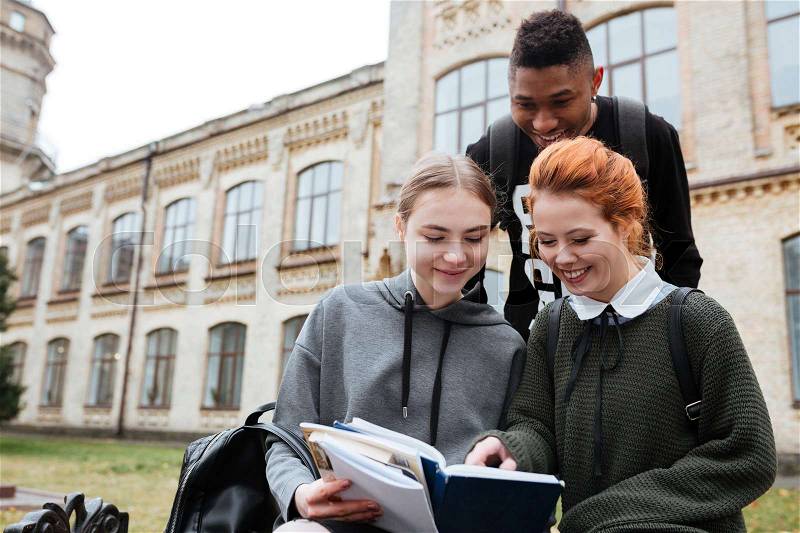 Multiethnic group of happy young people reading book outdoors at the unversity campus, stock photo