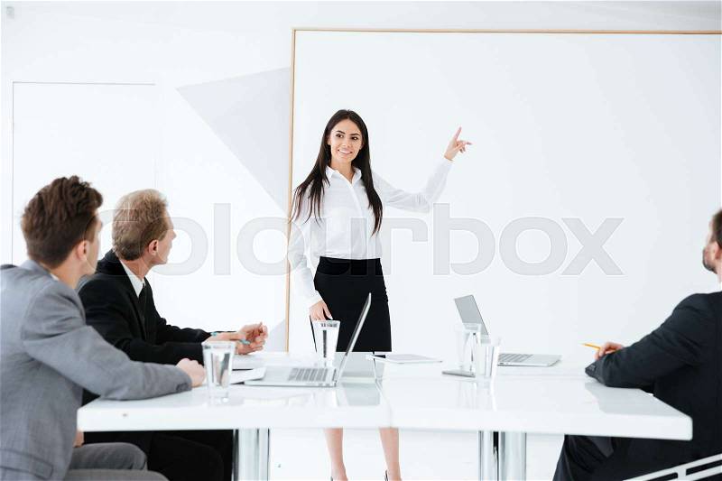 Woman standing near the board and pointing on board on conference with her colleagues in office, stock photo