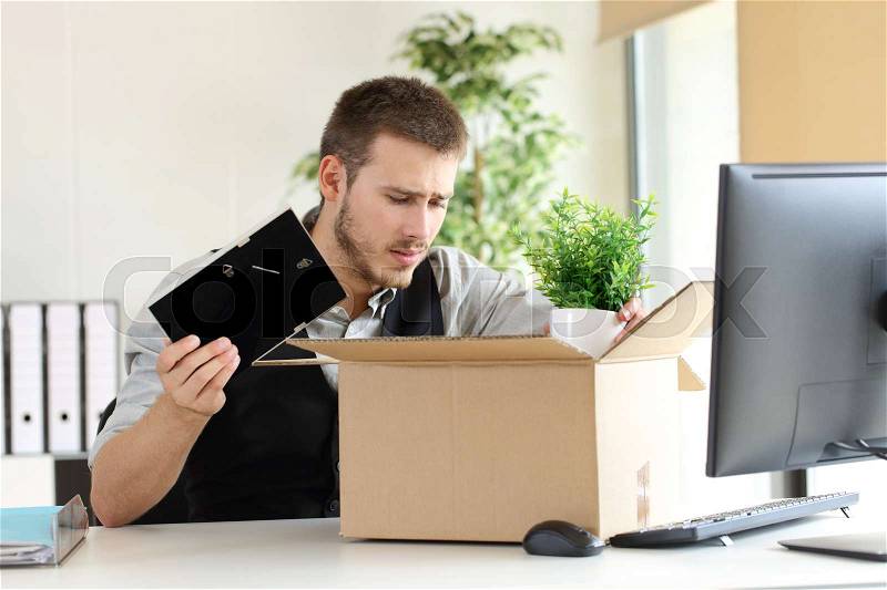 Sad fired businessman putting his belongings in a box from a desktop at office, stock photo