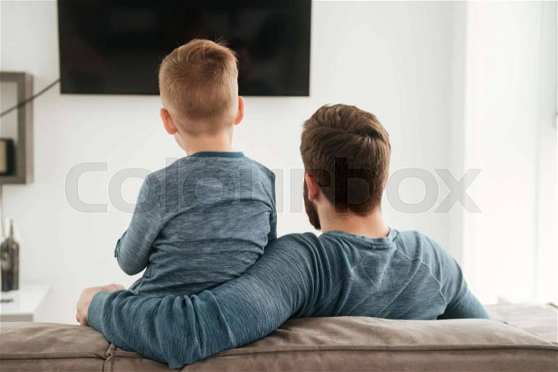 Back view photo of father watching TV with his little cute son, stock photo