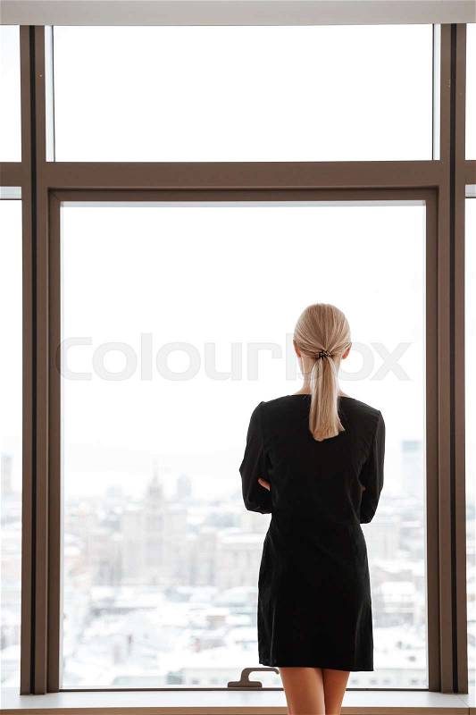 Back view image of young woman worker standing in office while looking at window, stock photo