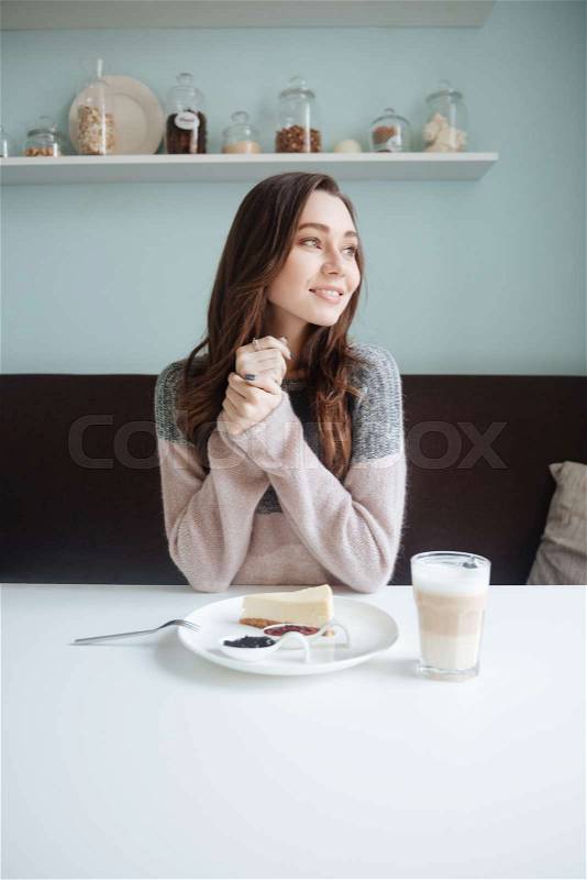 Picture of cheerful young lady sitting in cafe and having a breakfast with coffee and cake. Look aside, stock photo