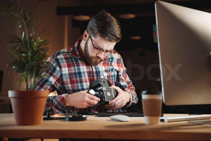 Portrait of a young bearded man repairing an old camera at his workplace, stock photo