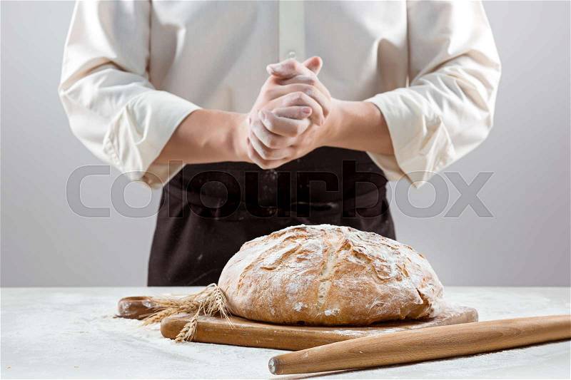 The hands of baker man and rustic organic loaf of bread - rural bakery on gray, stock photo