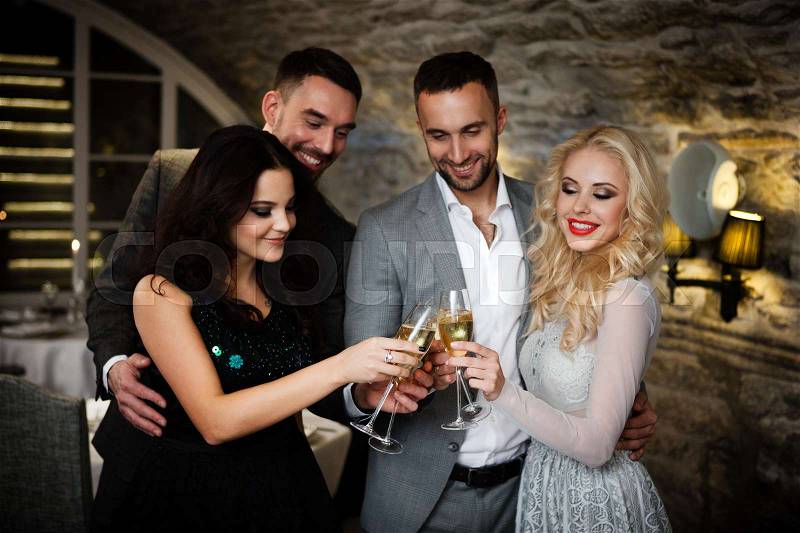 Four friends with champange glasses celebrating and toasting in restaurant, stock photo