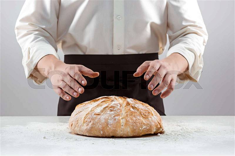 The hands of baker man and rustic organic loaf of bread - rural bakery on gray, stock photo