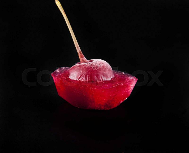 Red cherry is in ice on a black background closeup, stock photo