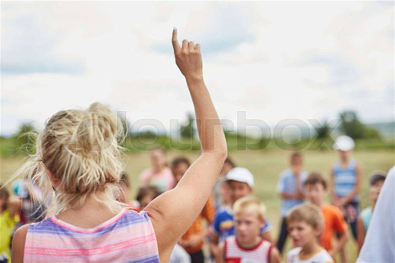 Young woman speaker in front of children crowd. Kids summer camp, stock photo