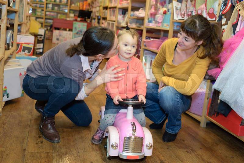 Mother and friend helping out daughter with toy truck, stock photo