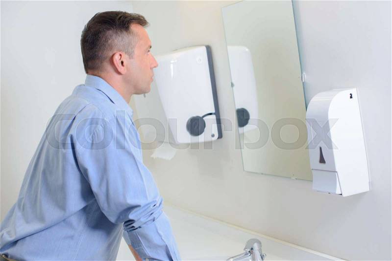 Man looking in mirror in restroom, stock photo