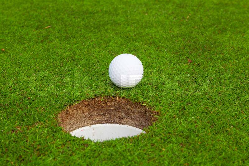 Golf ball on lip of cup. Golf ball on green grass in golf course, stock photo